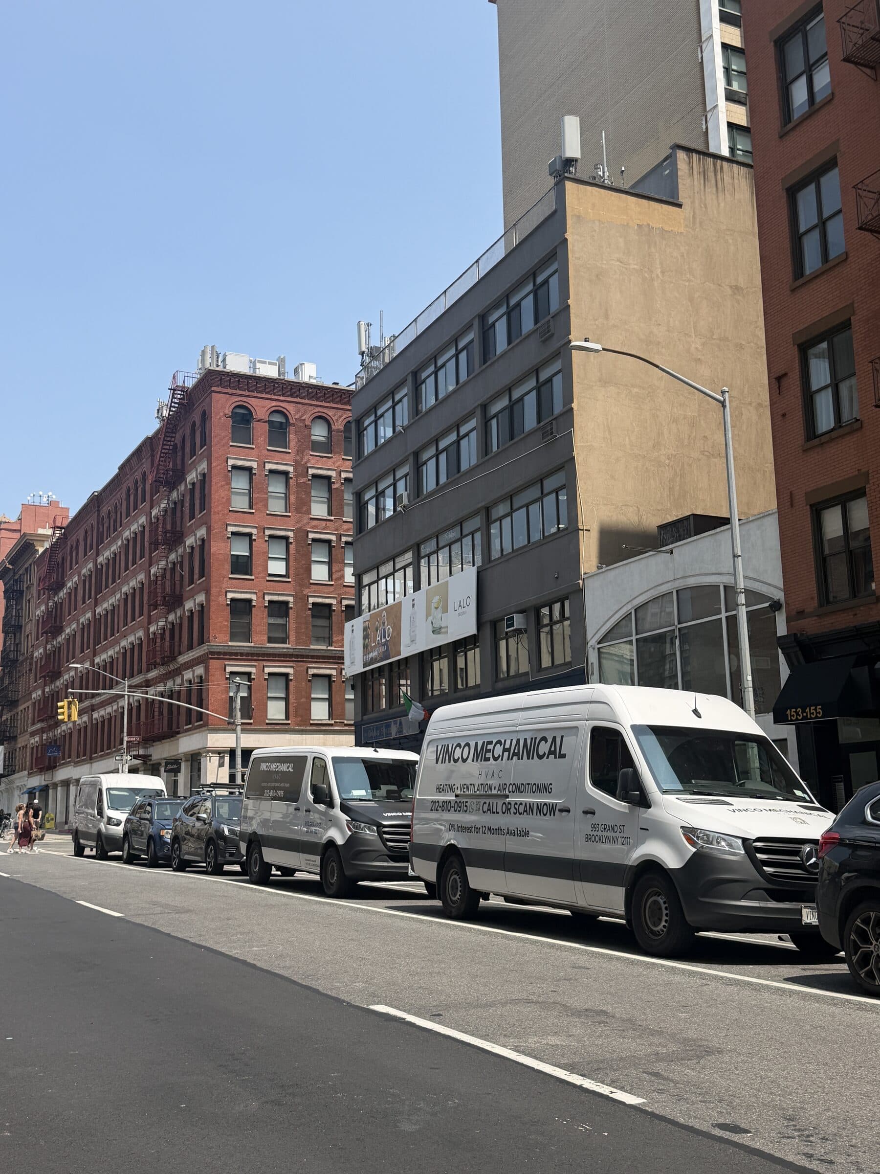 Two white Vinco Mechanical eSprinter electric vans in current 212 livery parked on Lafayette Street in SoHo during an emergency cooling call, cast-iron buildings and a billboard behind