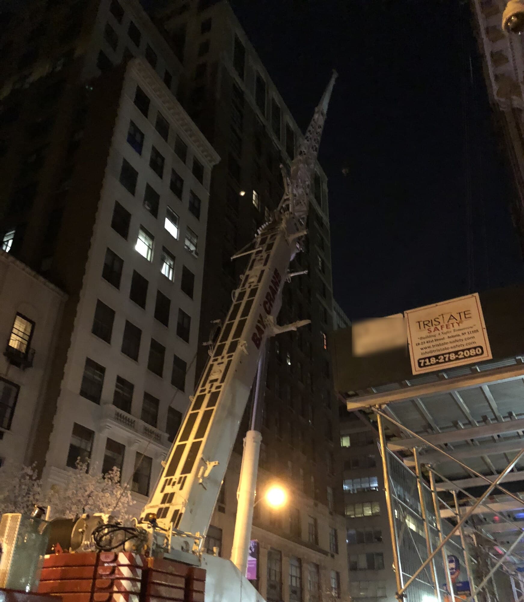 Bay Crane boom extended over a luxury apartment building at Madison Avenue and 37th Street at night during a permitted street closure