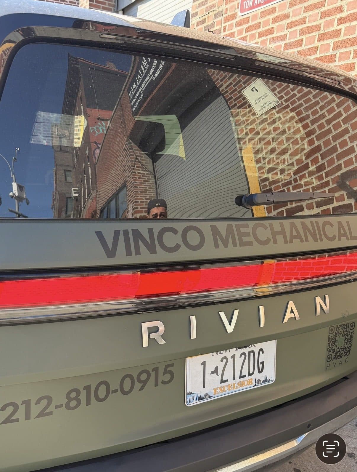 Close-up of the Rivian R1S tailgate showing the RIVIAN badge, VINCO MECHANICAL livery, the 212-810-0915 Manhattan line, and the 1-212DG vanity plate