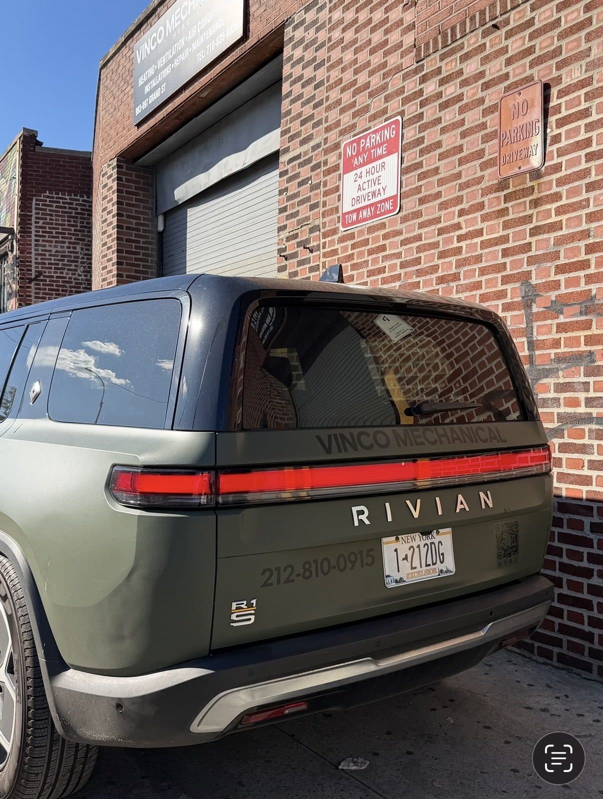 Olive-green Rivian R1S electric SUV in Vinco Mechanical livery parked at the 993 Grand Street shop, RIVIAN and R1S badges and Manhattan 212 number visible