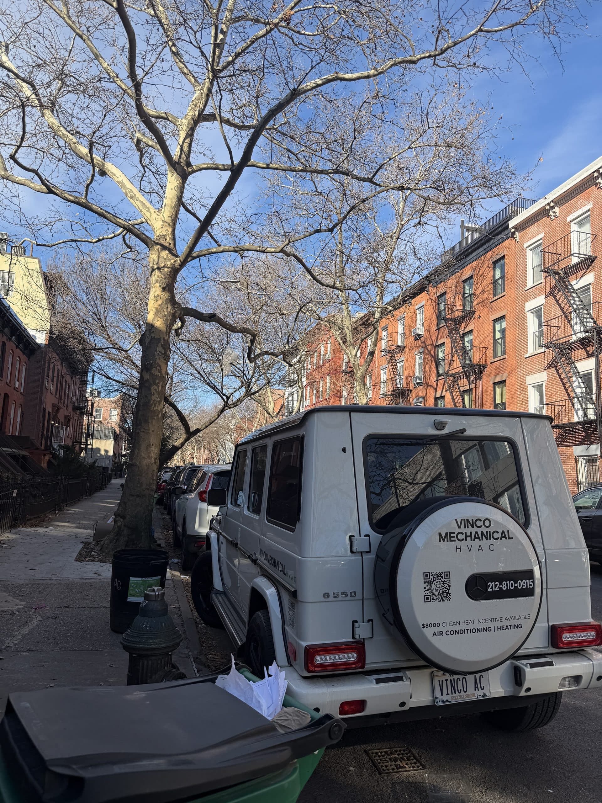 White Vinco Mechanical Mercedes G-Wagon parked on a Brooklyn brownstone block with brick rowhouses and fire escapes behind