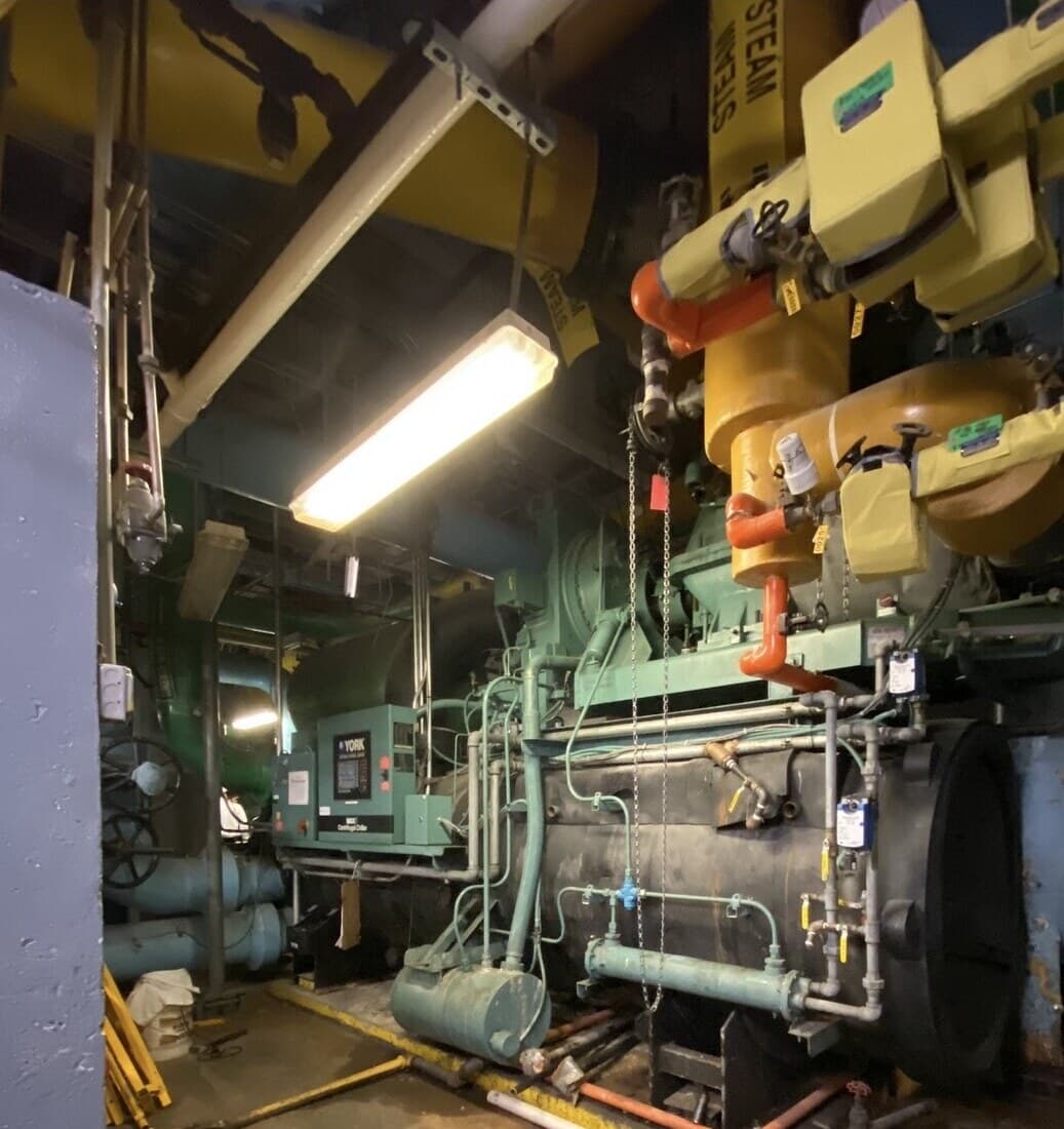 York centrifugal chiller with its control panel in a landmark Midtown tower basement plant room, steam and condenser piping overhead