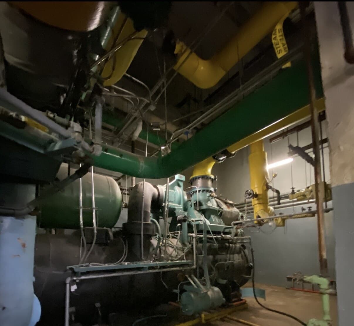 Centrifugal chiller compressor and condenser-water piping in a dark basement mechanical plant room of a landmark Midtown tower